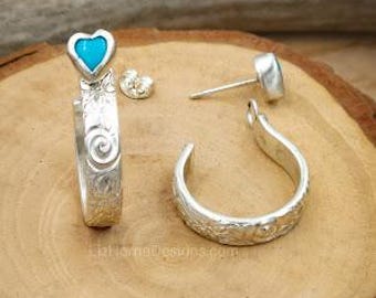 May include: A pair of silver hoop earrings with a turquoise heart charm. The earrings are on a wooden surface.