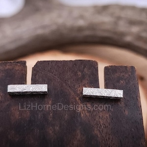 May include: Two silver bar earrings with a floral pattern on a dark brown wooden surface. LizHomeDesigns.com