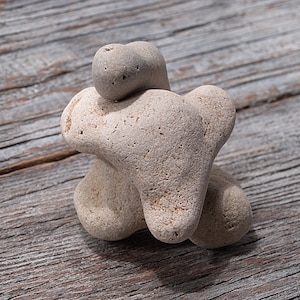 Könnte beinhalten: Eine Gruppe von drei glatten, hellgrauen Steinen, die in Herzform angeordnet sind. Die Steine liegen auf einer verwitterten Holzoberfläche.