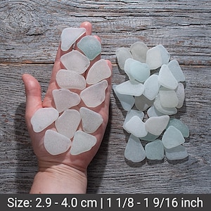 May include: A collection of sea glass pieces in various shapes and shades of white and pale green. The sea glass is displayed on a wooden surface. The size of the sea glass ranges from 1 1/8 to 1 9/16 inches.