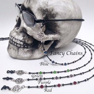 May include: Black eyeglass chains with a silver pentagram charm and colorful beads. The image shows chains in blue, green, purple, and red. The text "Fancy Chains" is visible.