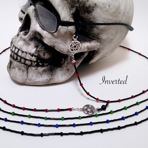 May include: Eyeglass chains with black cords and colorful beads. One chain features a silver pentagram charm. The image includes the word "Inverted". The chains are displayed on a skull.