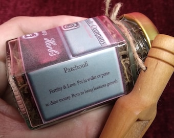 May include: A small glass jar with a brown twine tied around the lid. The jar contains dried herbs and has a label that reads "Patchouli Fertility & Love. Put in wallet or purse to draw money. Burn to bring business growth."
