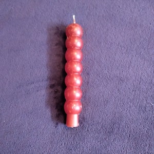 May include: A red candle with a beaded design. The candle is on a dark blue surface.