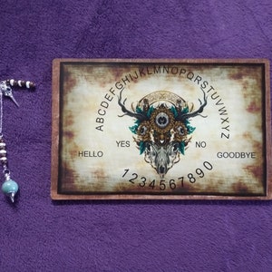 May include: A wooden Ouija board with a skull and floral design. The board has letters, numbers, and the words "Hello", "Yes", "No", "Goodbye".