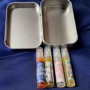 May include: A silver metal tin with four small glass bottles containing perfume. The bottles are labeled "Psychic Armor", "Asylum", "Come 2 Me", and "Born Empowered".