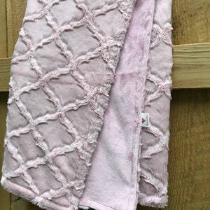 May include: A soft pink plush blanket with a trellis pattern. The blanket is folded in half and has a small tag that says "Love You"