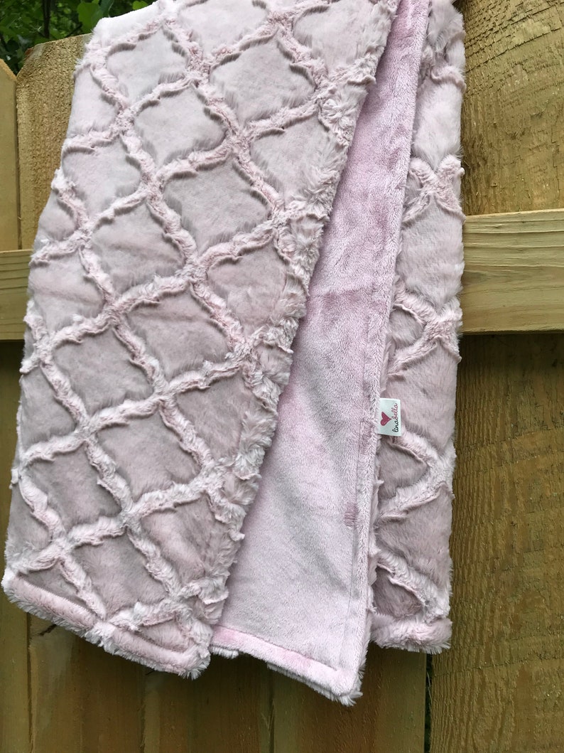 May include: A soft pink plush blanket with a trellis pattern. The blanket is folded in half and has a small tag that says "Love You"