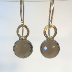 Könnte beinhalten: Ein Paar goldene Ohrringe mit Rauchquarz-Tropfen. Die Ohrringe haben ein schlichtes, elegantes Design.