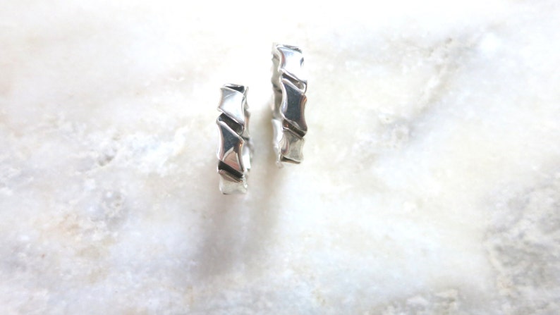 Op de afbeelding: Twee zilveren ringen met een uniek, geometrisch ontwerp. De ringen zijn gemaakt van glad, gepolijst metaal en hebben een licht getextureerd oppervlak.