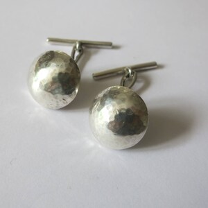 May include: A pair of silver cufflinks with a hammered, textured finish. The cufflinks have a simple, classic design.