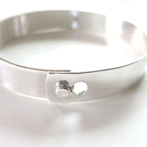 May include: A silver bangle bracelet with a simple design and a small, round, silver clasp.