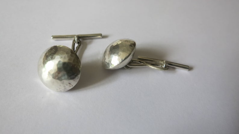 May include: A pair of silver cufflinks with a hammered, textured finish. The cufflinks have a simple, classic design.