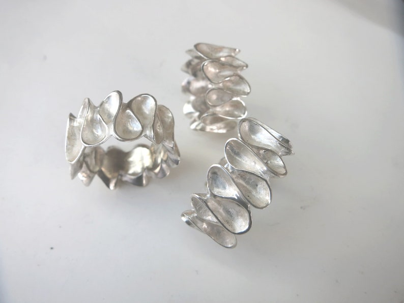 K&ouml;nnte beinhalten: Drei silberne Ringe mit einem einzigartigen, organischen Design. Jeder Ring besteht aus einer Reihe von miteinander verbundenen, tropfenf&ouml;rmigen Teilen.