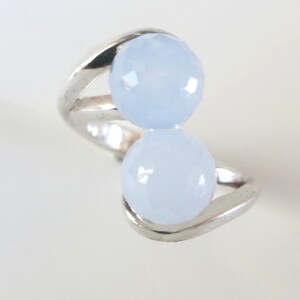 Può includere: Un anello d'argento con due pietre ovali di colore azzurro chiaro. L'anello ha un design unico con le pietre incastonate in una fascia attorcigliata.