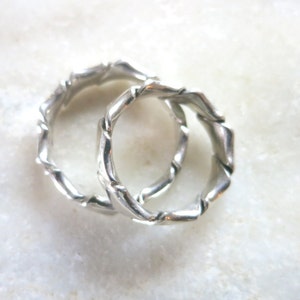 Op de afbeelding: Twee zilveren ringen met een gedraaid, getextureerd ontwerp. De ringen zijn in elkaar gehaakt en lijken van metaal te zijn.