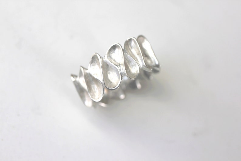 K&ouml;nnte beinhalten: Ein silberner Ring mit einem einzigartigen Design, das aus mehreren miteinander verbundenen tropfenf&ouml;rmigen Elementen besteht.