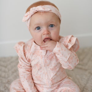 May include: A baby wearing a pink floral print long-sleeve onesie with a ruffled neckline and a pink floral headband.