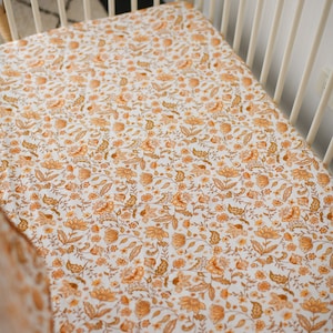 May include: A white fitted cot sheet with a floral pattern in shades of brown and orange.