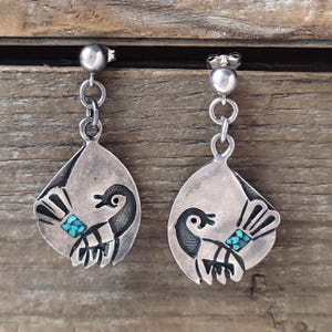 Puede incluir: Pendientes colgantes de plata con un diseño de ave estilizada y detalles turquesas. Los pendientes tienen un diseño de poste y cadena, con un colgante en forma de lágrima. El ave es negra, con una banda turquesa.