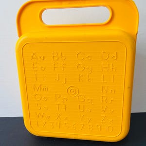 May include: A bright yellow vintage alphabet and number learning toy. The toy features the letters of the alphabet, both uppercase and lowercase, and the numbers 1 to 10. The toy has a handle for easy carrying.