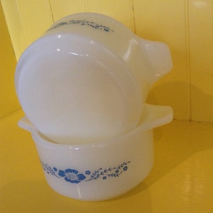 May include: Two white ceramic baking dishes with blue floral designs. The dishes are stacked on top of each other.