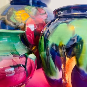 May include: Three ceramic vases with abstract floral designs in shades of blue, green, purple, and red. The vases are all different sizes and shapes.