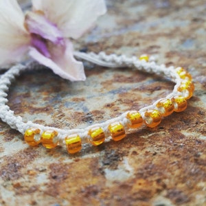 May include: A white cord bracelet with orange beads. The bracelet is on a rusty surface.