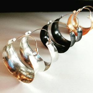 May include: A set of four hoop earrings in different metal finishes. The earrings are silver, black, copper, and gold. The hoops are thick and have a hammered texture.