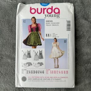 May include: A Burda Young sewing pattern for a Dirndl, a traditional Bavarian dress. The pattern packet features images of the finished dresses, with sizes listed in both UK and European measurements. The cover is white with pink and green accents.