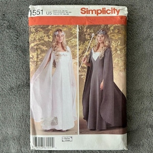 May include: Simplicity sewing pattern 1551 for fantasy-themed gowns. The pattern envelope features two women modeling the finished dresses. One gown is white with sheer sleeves, and the other is gray with a cape. The envelope has the Simplicity logo and size information.