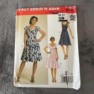 Könnte beinhalten: Ein McCall's Schnittmuster mit dem Titel "EASY stitch 'n save" mit Illustrationen von drei verschiedenen Kleidern. Das Muster enthält die Größen 8-16. Das Hauptkleid ist ein knielanges Kleid mit Kappenärmeln und einem blau-weißen geometrischen Muster.