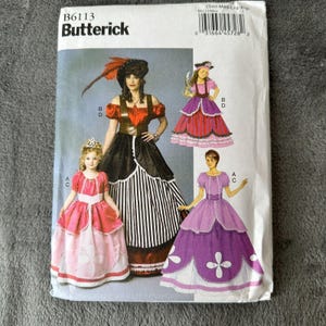 Puede incluir: Un sobre de patrón de costura Butterick con ilustraciones de cuatro diseños de disfraces diferentes. Los disfraces incluyen un vestido con temática pirata, un vestido estilo princesa y un vestido estilo victoriano. El sobre es blanco con el número de patrón B6113.
