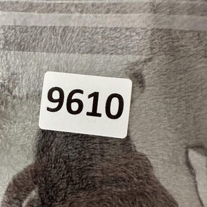 May include: A close-up of a gray and white patterned textile with a white label. The label displays the number "9610" in bold black font. The textile has a soft, plush appearance.