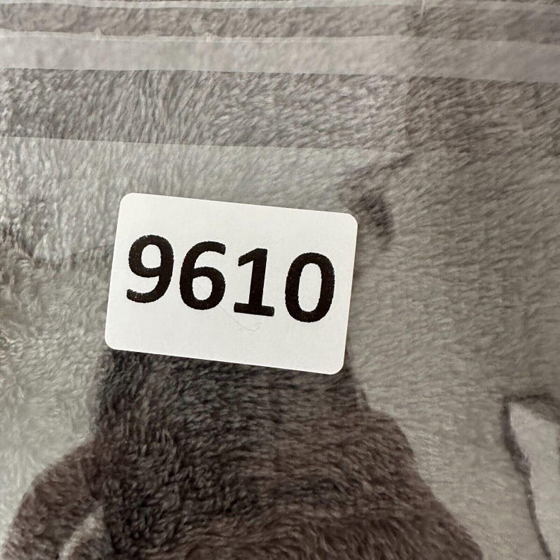 May include: A close-up of a gray and white patterned textile with a white label. The label displays the number "9610" in bold black font. The textile has a soft, plush appearance.