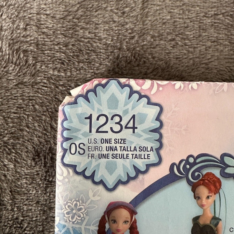 May include: A product box with the number "1234" in a snowflake design. The text "U.S. ONE SIZE" is visible, along with other size information in multiple languages. The box features illustrations of dolls.