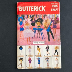 May include: A vintage Butterick craft pattern featuring doll designs. The cover is red with the Butterick logo and pattern details. The pattern showcases various doll outfits, including dresses and performance attire, with the designer's name, Wendy Everett, displayed.