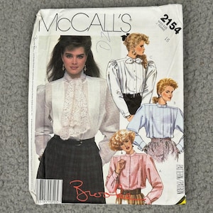Può includere: Un modello di cucito McCall's vintage, con una donna che indossa una camicetta bianca con colletto in pizzo. Il modello include illustrazioni di vari stili di camicette, con il numero 2154 visibile.