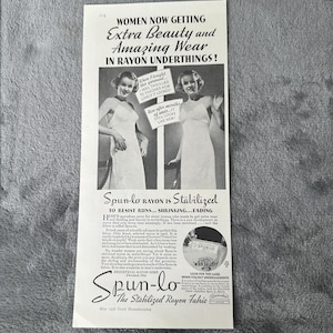 Könnte beinhalten: Eine Vintage-Werbung für Spun-lo-Rayon-Unterwäsche. Die Schwarz-Weiß-Anzeige zeigt zwei Frauen in Kleidern, mit Text, der die Beständigkeit des Stoffes gegen Laufmaschen, Einlaufen und Ausbleichen hervorhebt. Die Anzeige enthält den Text "Extra Beauty and Amazing Wear."