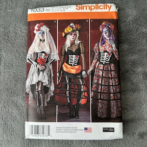 May include: Simplicity sewing pattern 1033 R5 features three Day of the Dead costume designs. The costumes include skeleton-themed bodices, skirts, and floral headpieces. The pattern is designed and printed in the USA.