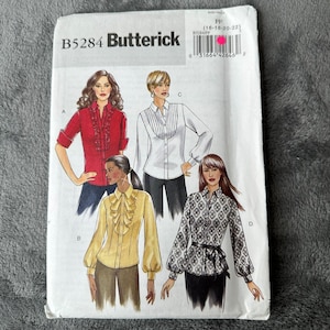 May include: Butterick sewing pattern B5284 featuring four shirt variations. The illustrations show a red ruffled shirt, a white pleated shirt, a yellow ruffled shirt, and a patterned shirt with a belt. The package includes size range FF 16-18-20-22.