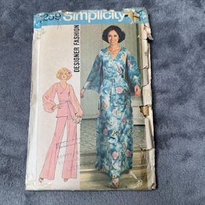 May include: Vintage Simplicity Designer Fashion sewing pattern. The pattern features a woman in a long, flowing blue floral dress with wide sleeves and a matching belt. The pattern also shows a pink jumpsuit. The pattern is labeled #7259.