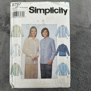 May include: A Simplicity sewing pattern envelope featuring images of women's shirts. The envelope has the number 8797 and the Simplicity logo. The shirts are in various styles, including a lace shirt and a blue striped shirt.