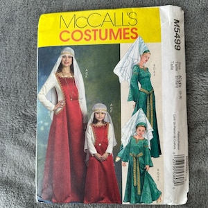 Może przedstawiać: Wzór szycia McCall's Costumes przedstawiający sukienki w stylu średniowiecznym dla dorosłych i dzieci. Okładka wzoru przedstawia ilustracje kostiumów w kolorze czerwonym, białym i zielonym. Rozmiar wzoru jest dla dzieci w wieku 3-8 lat.