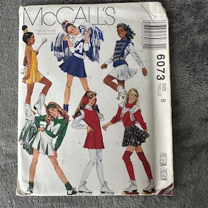 May include: A sewing pattern for girls' clothing, featuring five different outfits. The pattern is for size 8 and includes a skirt, a dress, a cheerleading outfit, and a sweater. The pattern is from McCall's and the pattern number is 6073.