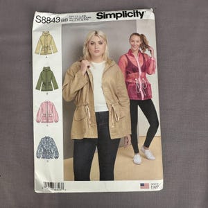 May include: Simplicity sewing pattern S8843 featuring jacket designs. The pattern includes illustrations of jackets in various colors, including tan, green, pink, and floral. The pattern is sized for US L-XXL and includes the text "Since 1927".