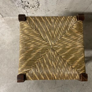 K&ouml;nnte beinhalten: Quadratischer Stuhlsitz mit einem nat&uuml;rlichen, hellbraunen Webmuster. Der Sitz besteht aus eng gewebtem Stroh oder &auml;hnlichem Material mit dunkelbraunen Holzecken. Draufsicht.
