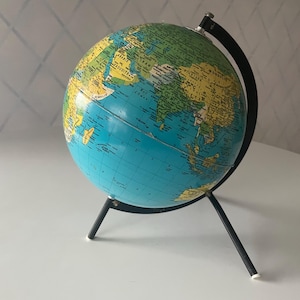 Peut inclure: Un globe vintage avec des océans bleus et des continents verts et jaunes. Il est monté sur un support en métal noir à trois pieds. Un outil éducatif classique.