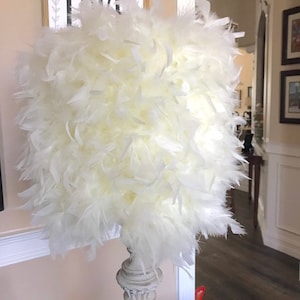 Puede incluir: Una pantalla de l&aacute;mpara de plumas blancas con una base de l&aacute;mpara blanca de estilo columna desgastada.
