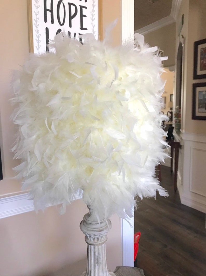 Puede incluir: Una pantalla de l&aacute;mpara de plumas blancas con una base de l&aacute;mpara blanca de estilo columna desgastada.